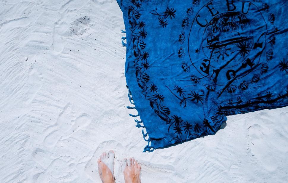 Free Image of Blue beach towel on white sand with bare feet visible 