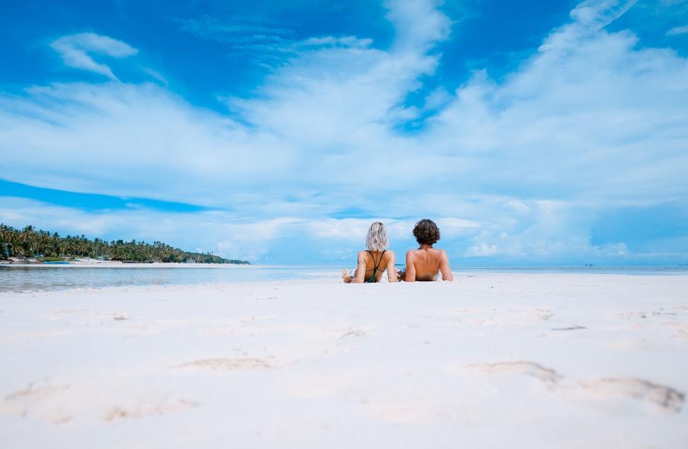 Free Image of Two people relaxing on a pristine sandy beach 