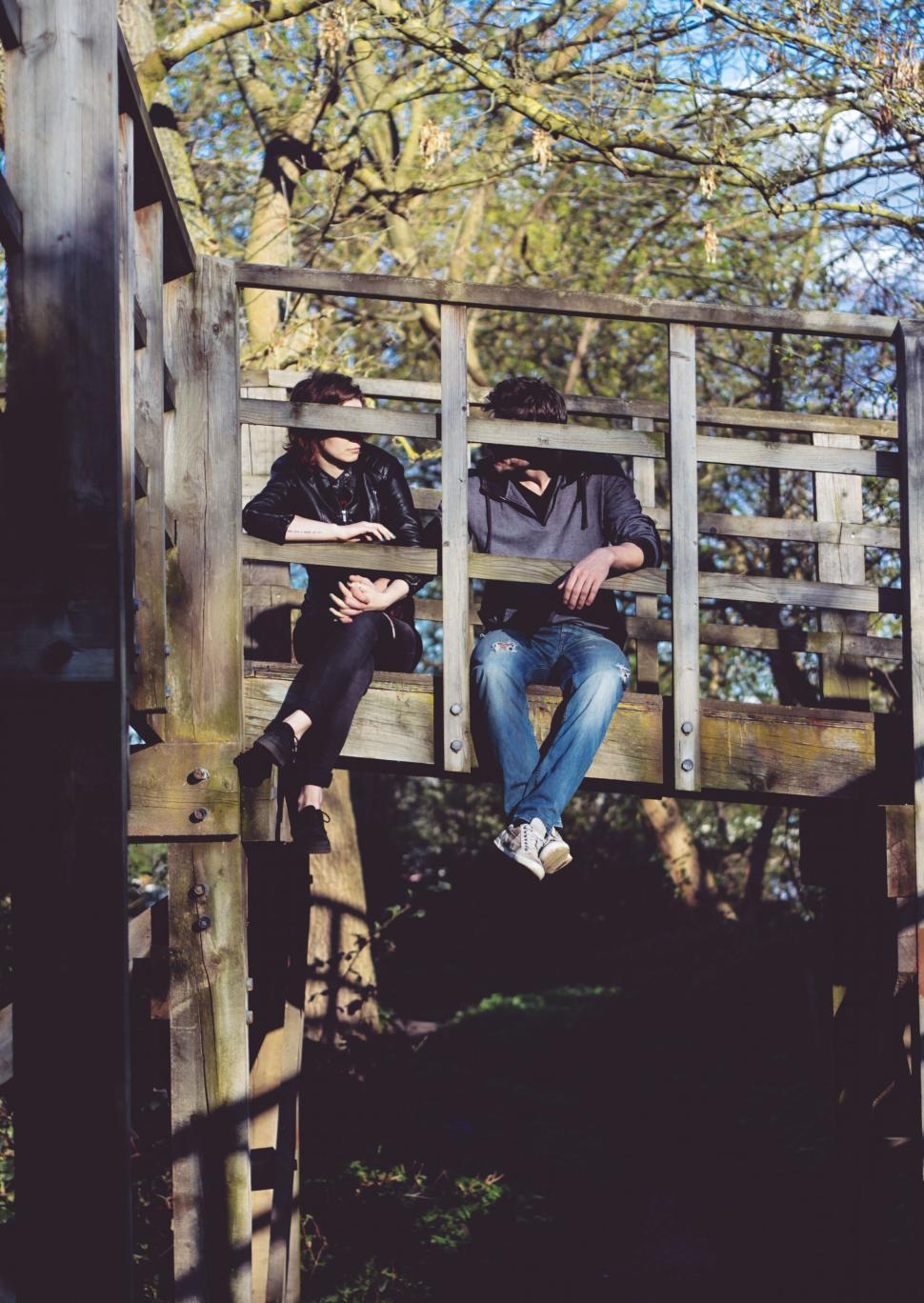 Free Image of Two people relaxing on a wooden bridge in nature. 