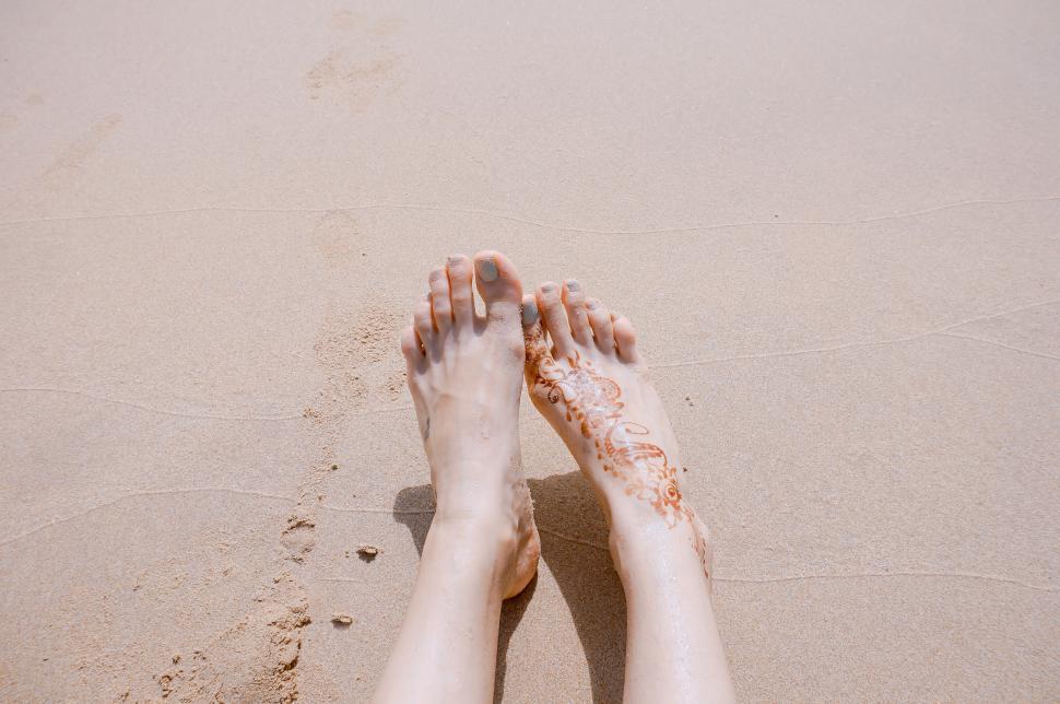 Free Image of Feet with henna on sandy beach on a sunny day. 