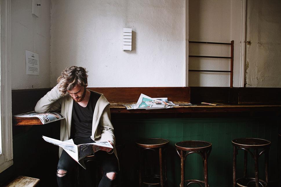 Free Image of Person reading newspaper in cozy cafe with wood stools 
