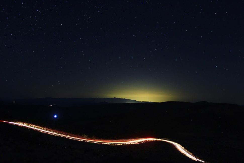 Free Image of Night sky with star trails above winding road 