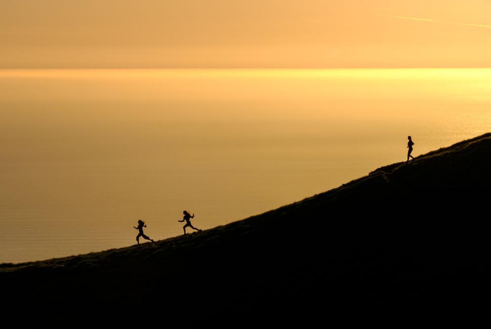 Free Image of Silhouetted runners ascend hill against golden sunset. 