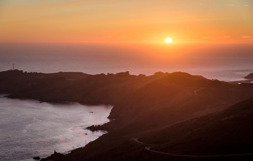 Free Image of Sunset over coastal hills with winding road and calm sea. 