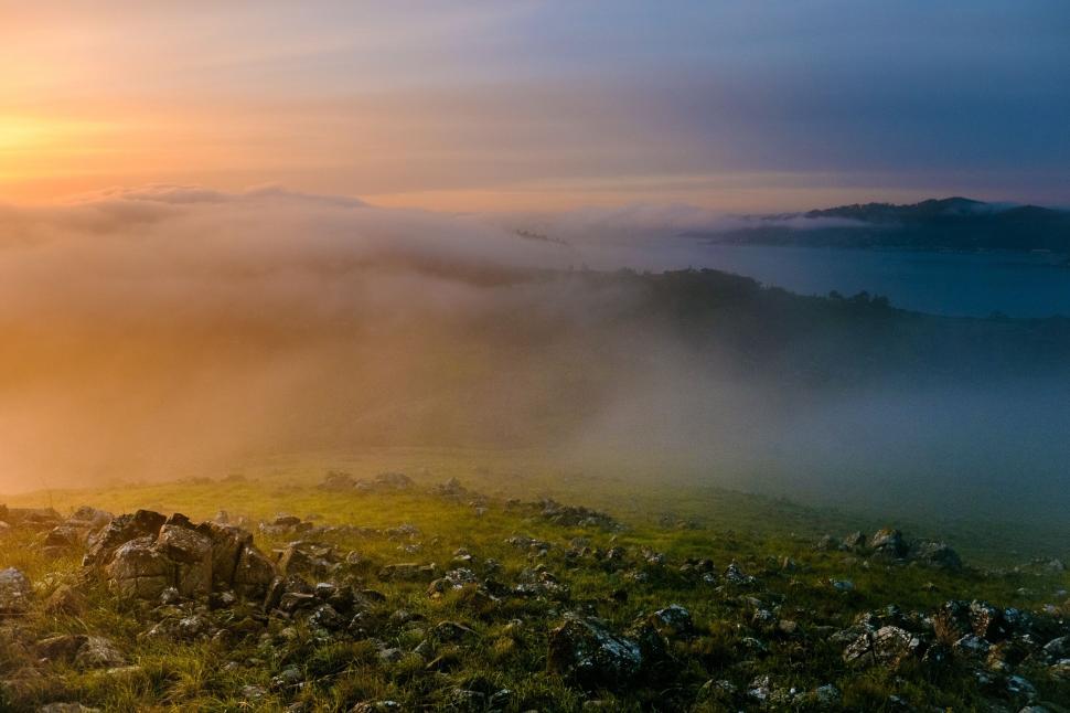Free Image of Morning fog blankets grassy hills under sunrise. 