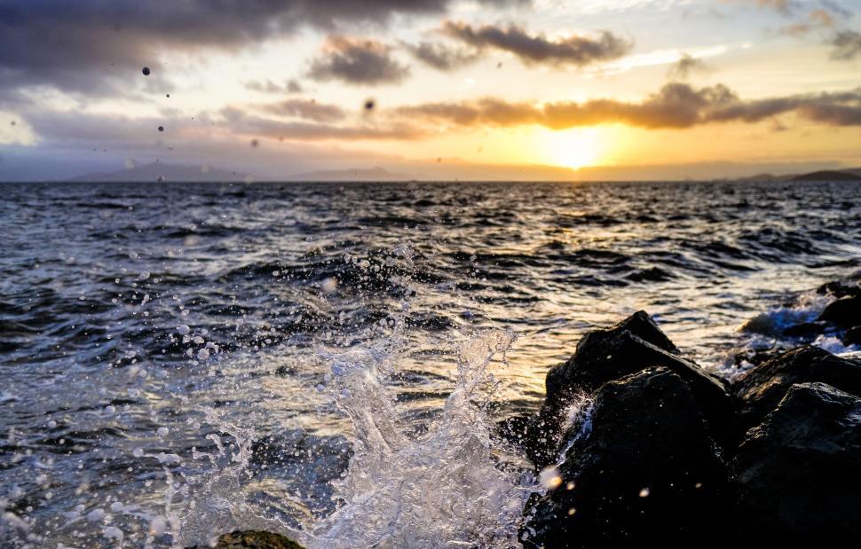 Free Image of Waves crashing on rocky shoreline during sunset. 