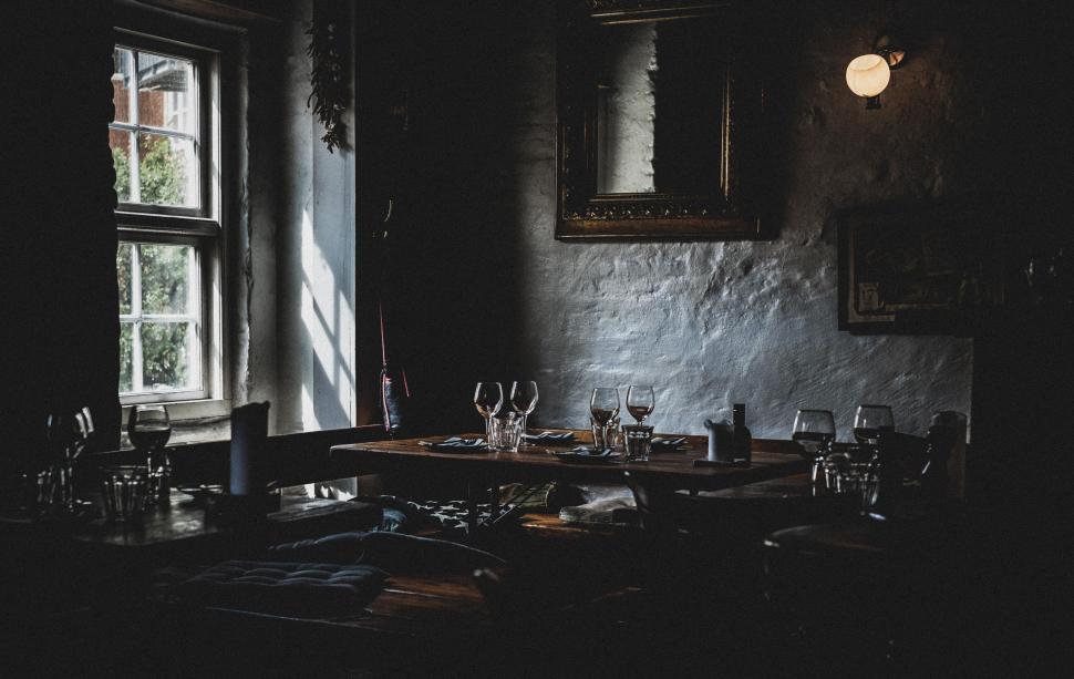 Free Image of Dimly lit rustic restaurant with empty tables by window. 