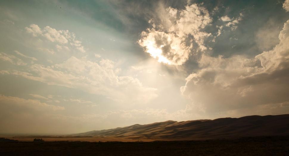 Free Image of Sunlight piercing through clouds over desert landscape. 