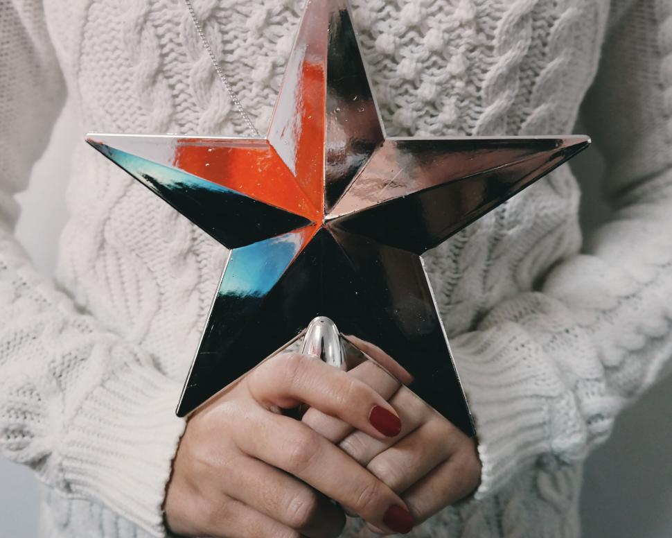 Free Image of Person holding a shiny star ornament with red nails 
