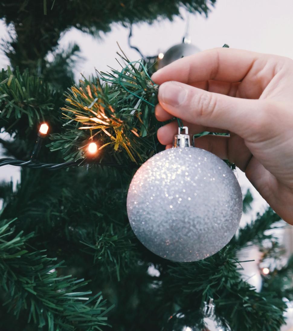 Free Image of Hand decorating a Christmas tree with silver bauble 