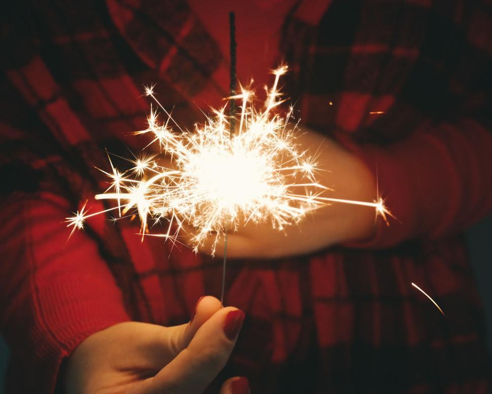 Free Image of Sparkler lit in hand with plaid shirt in background 