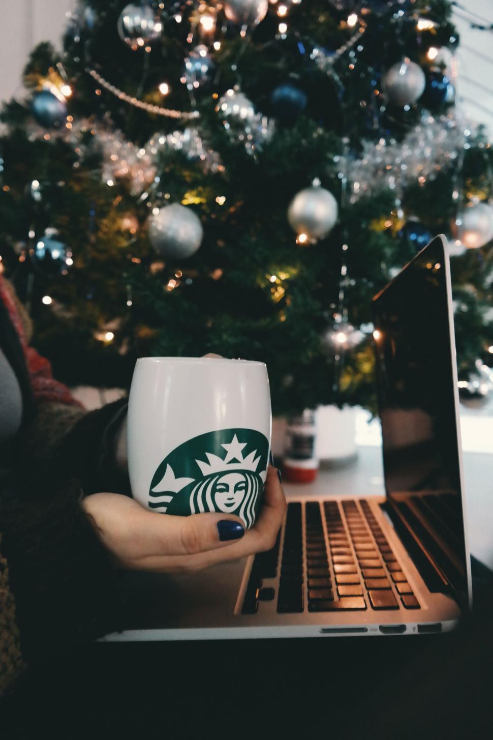 Free Image of Woman holding Starbucks mug by a Christmas tree 