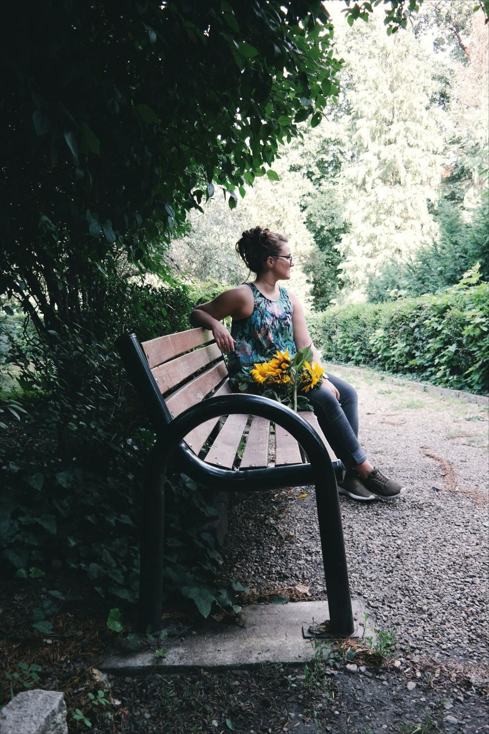 Free Image of Person sitting on park bench holding bouquet of sunflowers 