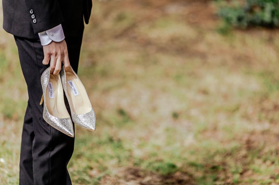 Free Image of Groom holding bride s sparkling shoes near grass 
