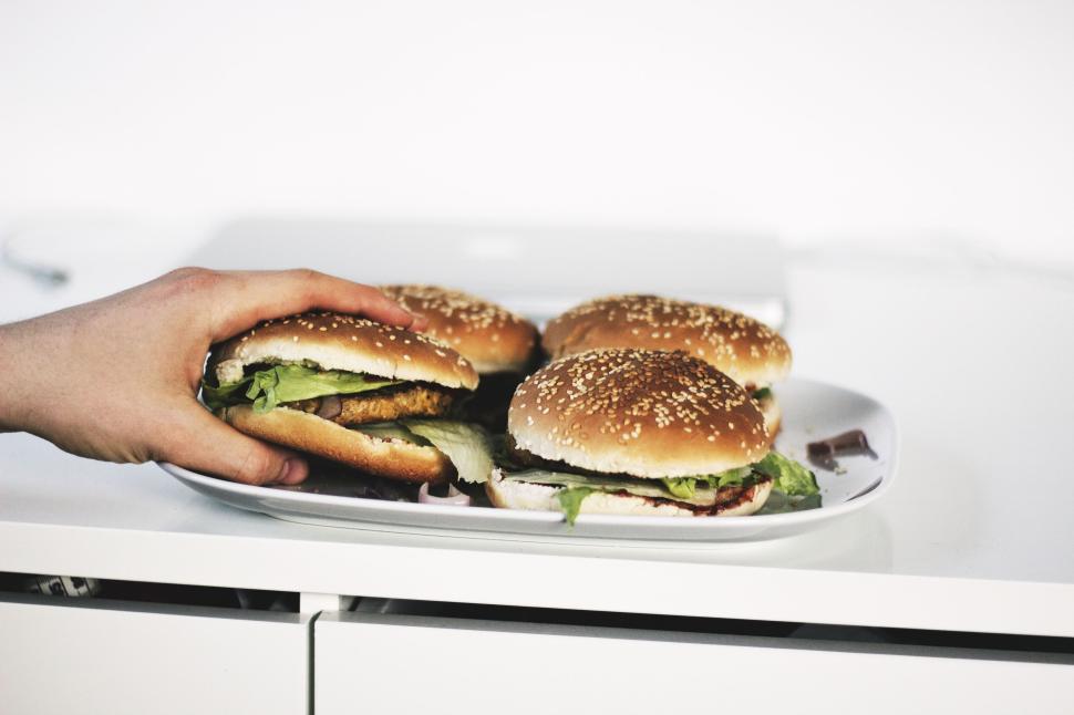 Free Image of Hand reaching for burgers on a white table surface. 
