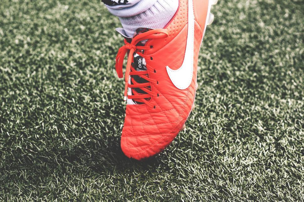 Free Image of Close-up of red soccer cleats stepping on green grass. 