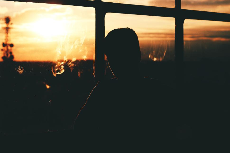 Free Image of Silhouette of a person watching a sunset through window 