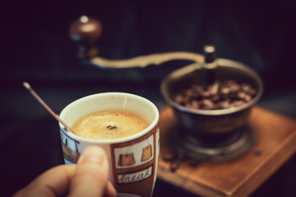 Free Image of Holding a cup of coffee with old-fashioned grinder nearby 