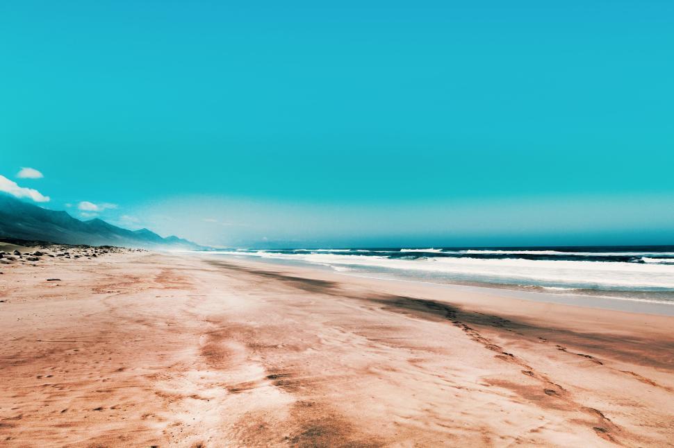 Free Image of Wide-open beach with clear sky and distant waves. 