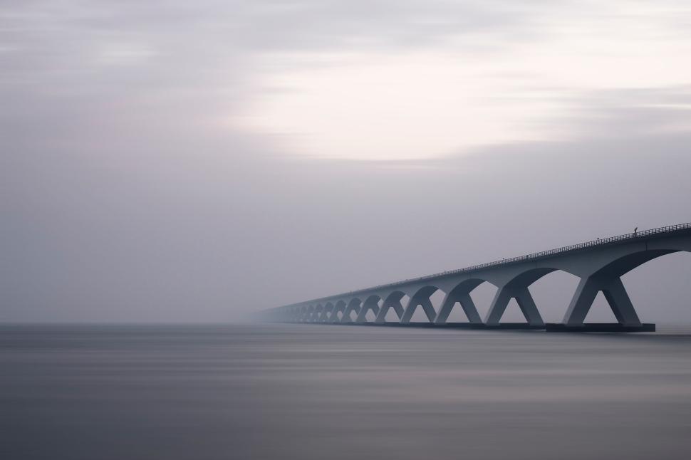 Free Image of Long bridge stretching into the fog over calm water. 
