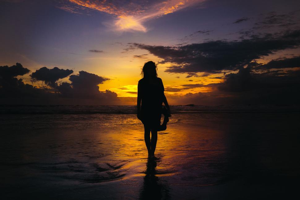 Free Image of Person walking on beach at sunset, silhouette glowing. 