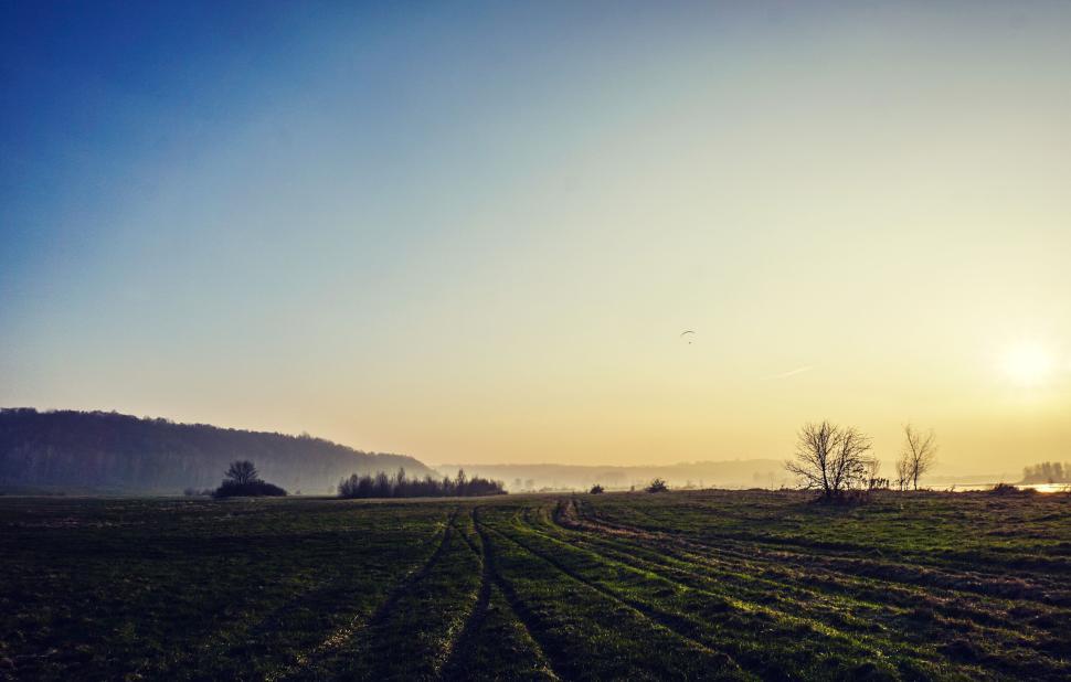 Free Image of Sunset over scenic field with visible tire tracks, 