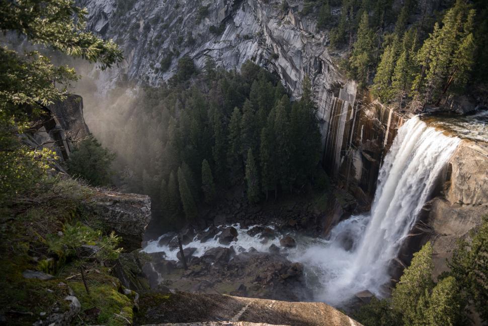 Free Image of Waterfall cascading down rugged cliffs with forest. 