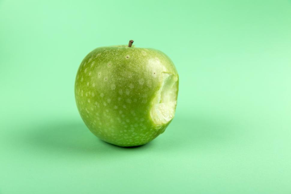 Free Image of Green apple with a bite taken out on green background 
