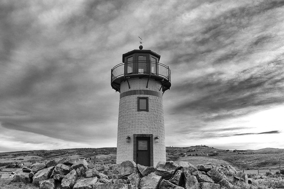 Free Image of Lighthouse under dramatic sky standing amidst rocky terrain. 