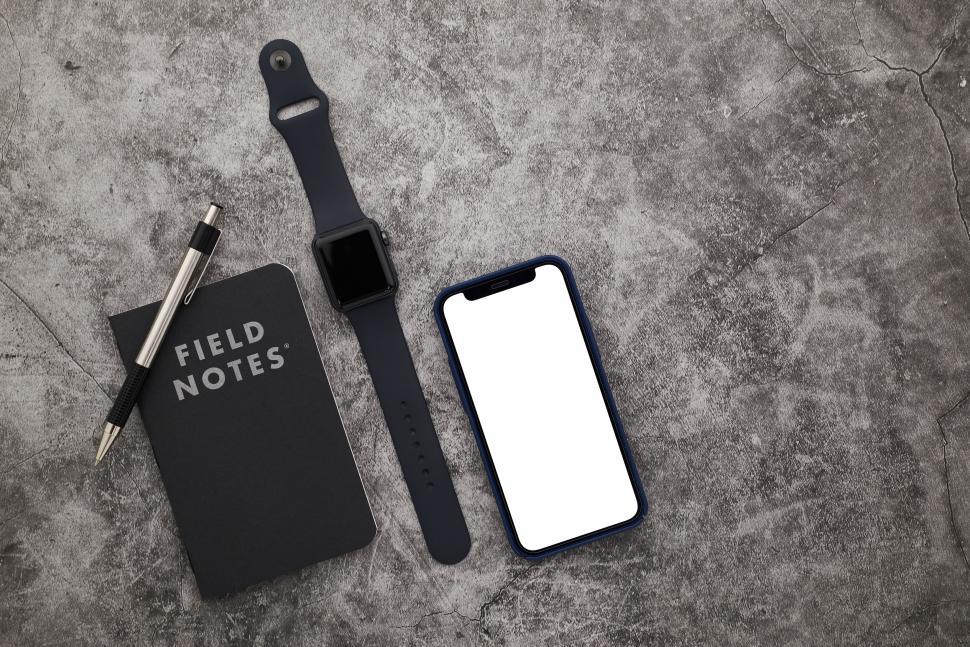 Free Image of Smartwatch, phone, notebook, and pen on grey surface. 