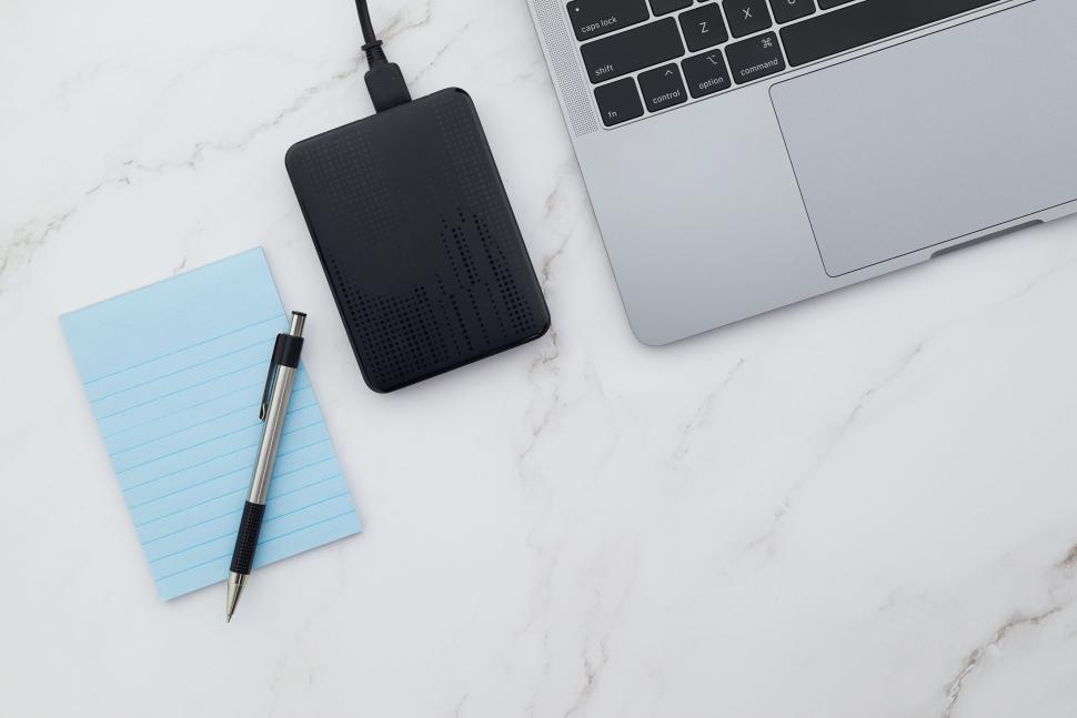 Free Image of Laptop and external drive with blue notepad and pen 