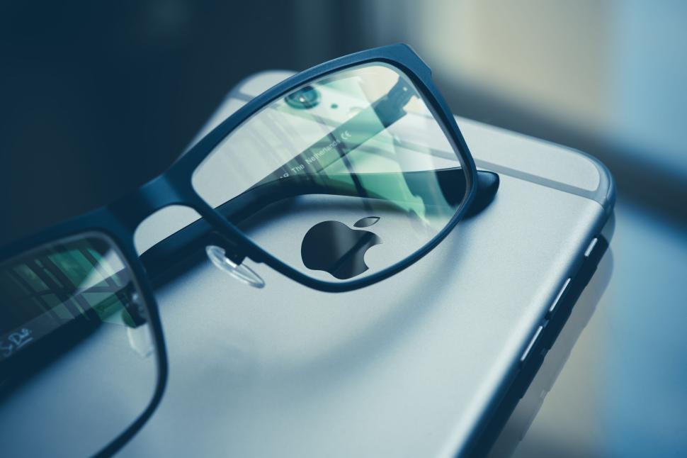 Free Image of Glasses resting on an Apple iPhone on a blue background. 