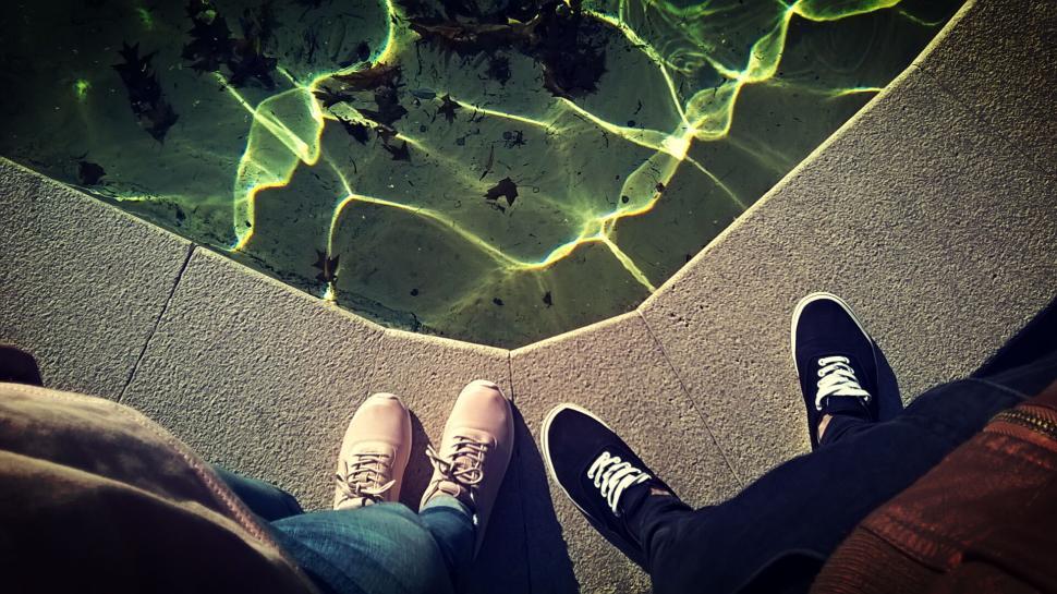 Free Image of Two pairs of legs with shoes, standing by a lit pool edge 