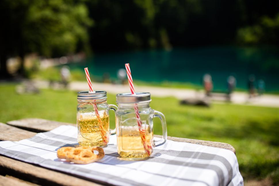 Free Image of Two mason jars with drinks on tablecloth by a lake 