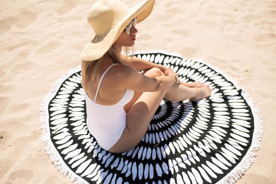 Free Image of Woman on a sandy beach sitting on a round beach towel 