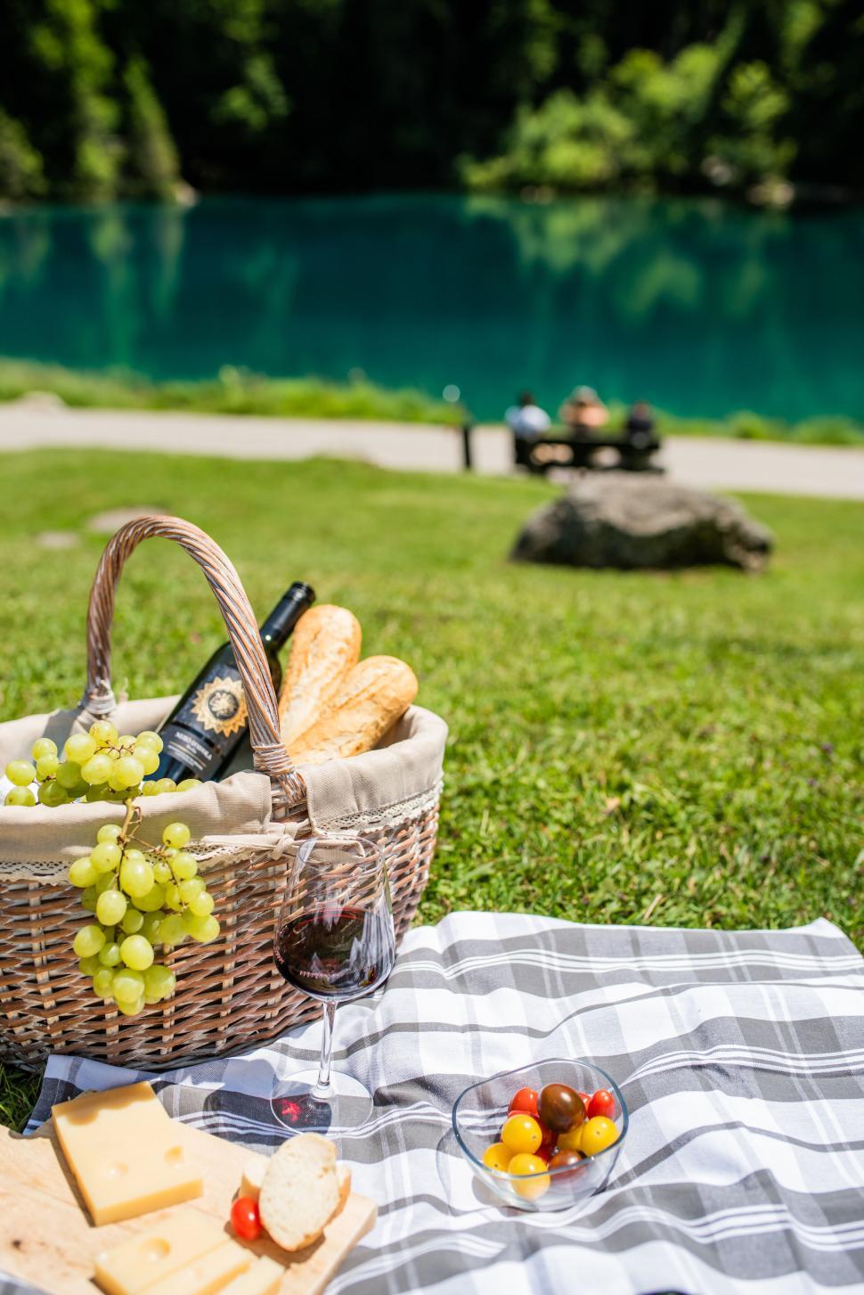 Free Image of Picnic setup with wine, cheese, bread by tranquil lake 