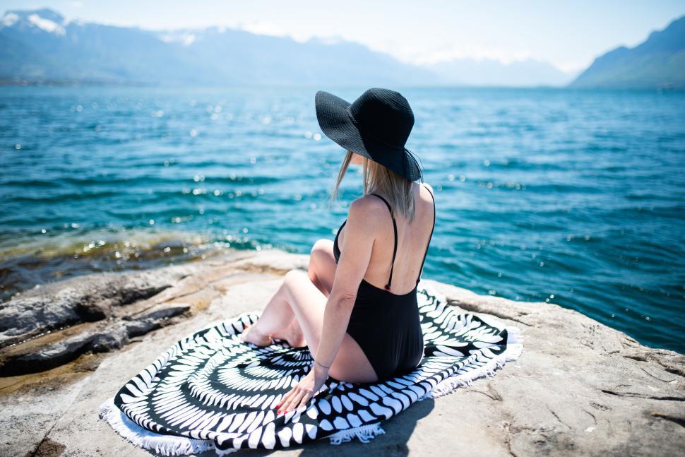 Free Image of Woman in swimsuit and hat sitting by a mountain lake 