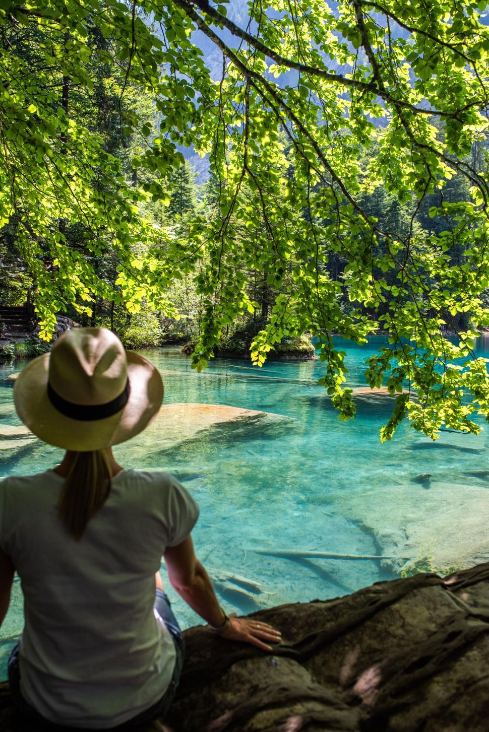Free Image of Person in hat enjoying nature by a clear blue water body 