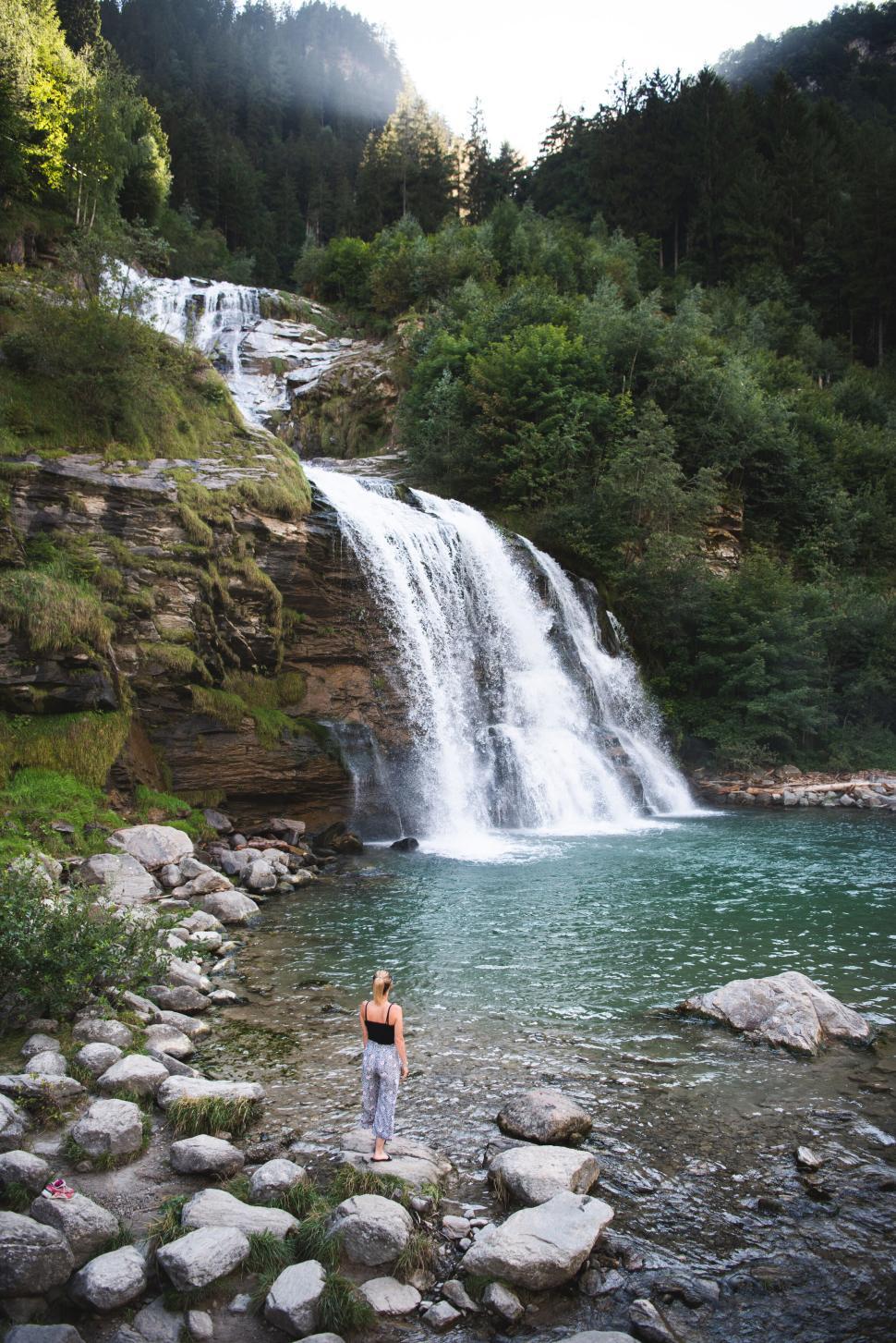 Free Image of Woman standing on rocks by a beautiful waterfall 