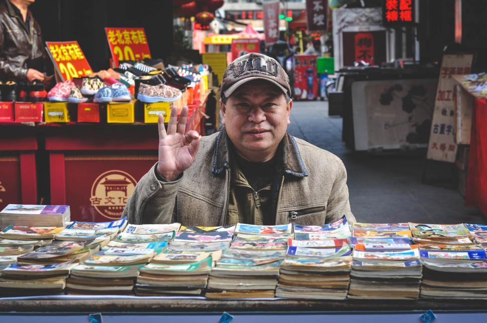 Free Image of Man selling books with friendly gesture in street market 