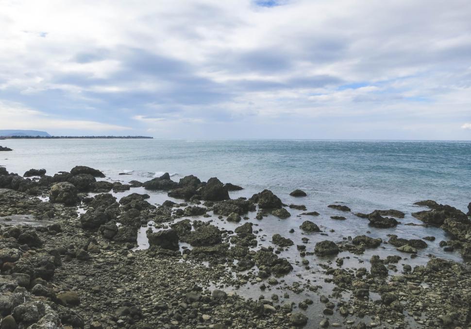 Free Image of Rocky coastline with clear blue sea and cloudy sky. 