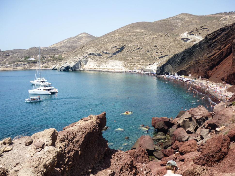 Free Image of Rocky cliffside overlooking a crowded beach with boats 