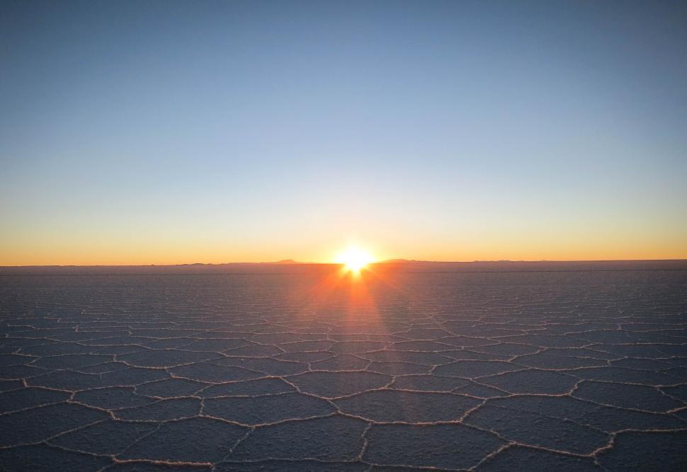 Free Image of Sunrise over vast, patterned salt flat landscape 