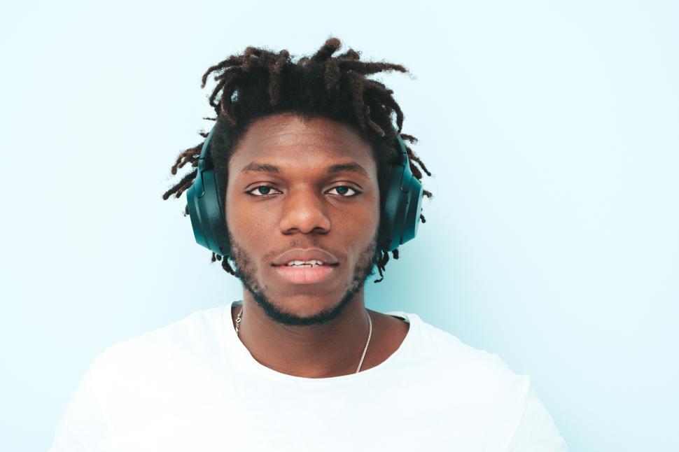 Free Image of Man with headphones looking at camera against blue wall. 