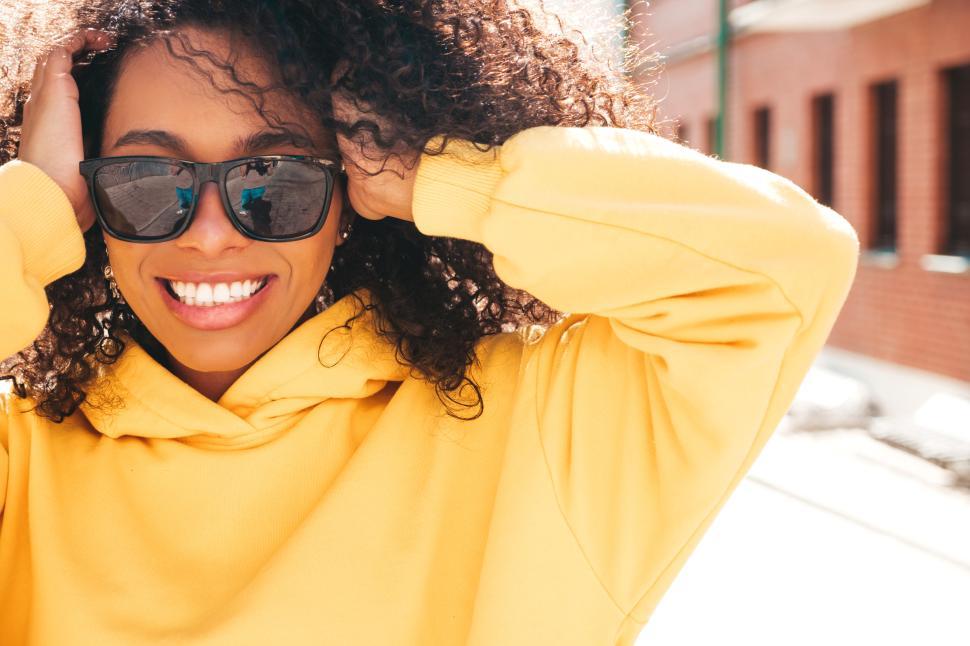 Free Image of Individual in yellow hoodie adjusting hair outside. 