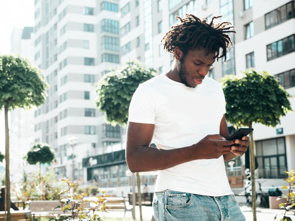 Free Image of Man in white t-shirt using smartphone in urban area. 