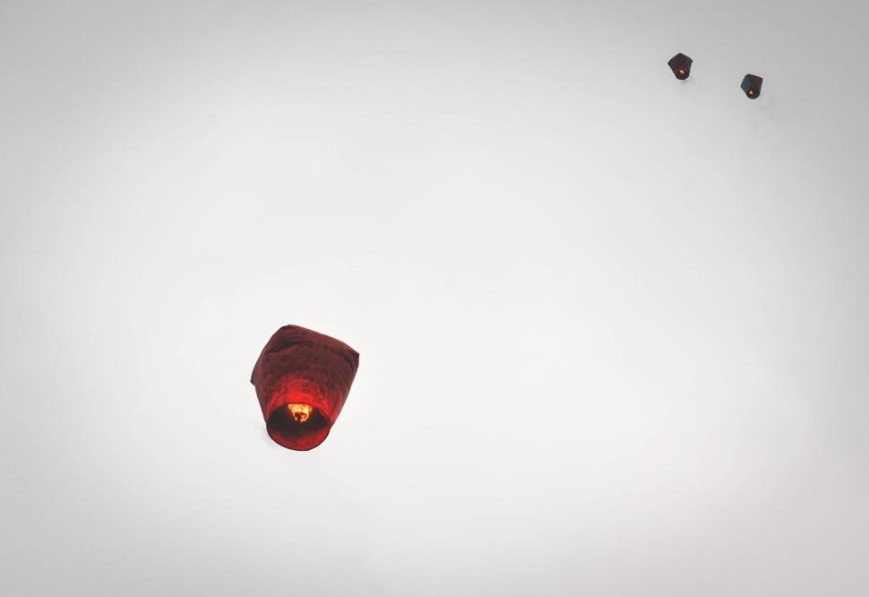 Free Image of Red paper lanterns floating in a clear, grayish sky 