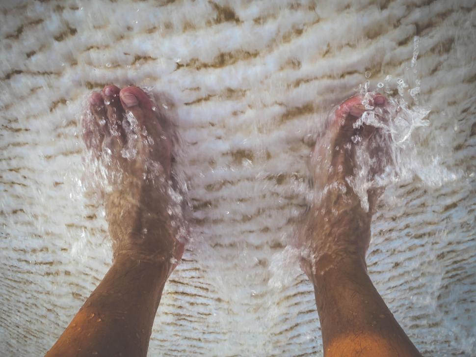 Free Image of Feet in flowing water over a sand-like textured surface. 
