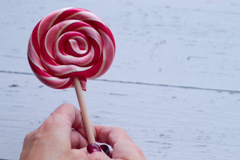 Free Image of Hand holding red and white lollipop on wooden table 
