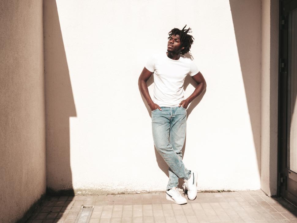 Free Image of Man leaning against wall in sunlight with hands in pockets 